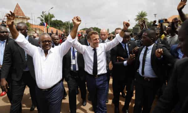 French President Emmanuel Macron (C) and Guinea-Bissau’s President Umaro Sissoco Embalo (L) gesture to the crowd in front of the Presidential Palace in Bissau in July 2022.