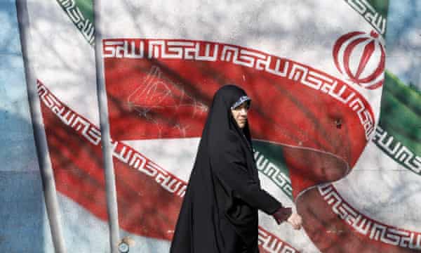 An Iranian woman walks next to a wall painting of Iran’s national flag on a street in Tehran.