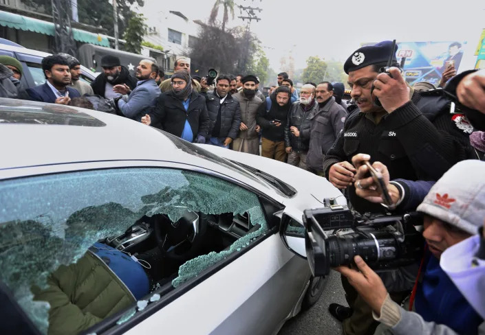 Police officer and journalists gather around the car of local journalist Husnain Shah at the site of shooting incident, in Lahore, Pakistan, Monday, Jan. 24, 2022. Unidentified gunmen riding on a motorcycle shot and killed Shah in the eastern city of Lahore on Monday before fleeing the scene, a police official and representatives of journalists said. (AP Photo/K.M. Chaudary)